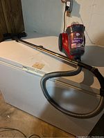 Full view of Dirt Devil Featherlite canister vacuum on white chest freezer with attached wand and hose showing overall setup and size.