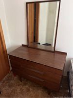 Photo showcasing wood dresser with mirror leaning on top, visible scratches on wood surface, angled legs.