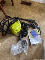Electric Sun Joe power washer with cords, spray gun, attachments, and instructions laid out on carpet.