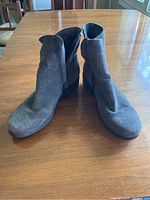 Front and inner side view of the grey suede La Canadienne winter boots placed on a wooden surface with visible slight wear marks on the toes and suede material.