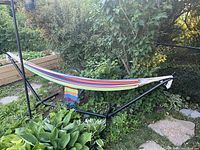 Hammock fully set up on black metal stand in backyard, colorful striped fabric visible