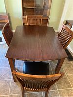 Full view of the wooden table with four chairs showing the polished wood surface and chair arrangement.