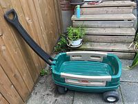 Full side view of green and beige Little Tikes wagon showing black handle and wheels