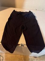 Full view of the Lululemon Capri pants laid flat showing entire length and shape in light shadow, illustrates overall condition and color that looks dark purple/bluish.