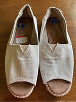 Top front view of a pair of beige canvas Toms shoes, showing the toe opening and insole labels indicating size 7 1/2.