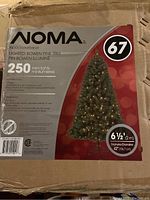 Close-up photo of the Noma Christmas tree box showing brand, model, dimensions, light count, and branch tips.