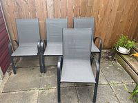 Four sling back patio chairs arranged outside on a stone patio, showing overall good condition with some rust spots.