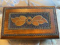 Top view of box lid showing flower with leaf engraving and detailed border around the flower panel.