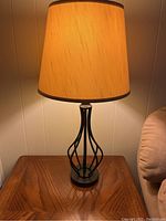 Table lamp on wooden table against paneled wall, showing the lamp design and shade.