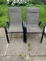 Front view of two black metal frame patio chairs with sling mesh seats and backs, showing overall condition and design.