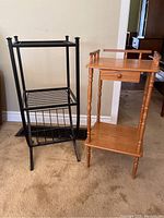 Photo showing both side tables together; black iron table with curved base and two shelves on left, wooden side table with drawer and turned legs on right.