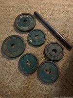 Photo of 6 vintage green painted cast iron barbell weight plates and one metal bar laid on carpet.