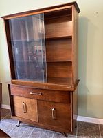Front view of vintage wooden China cabinet showing glass sliding doors, drawer, and bottom doors with brass handles.