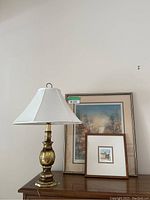 View of the brass lamp and two framed artworks on a wood surface against a wall