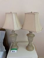 Pair of beige lamps with fabric shades on a white table, showing details of base and shades.