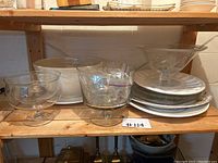 Shelf with large clear glass serving bowls and platters, white ceramic plates and bowl.