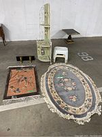 All items in the lot arranged on a concrete floor showing the rugs, shelving unit, wall shelf, and step stools.