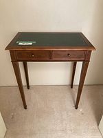 Front view of small wooden desk with two drawers and a green leather top inset with gold tooling.