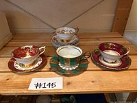 Three teacups each paired with a saucer on wooden shelf, plus stack of extra saucers in background
