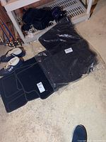 View of the set of black Mercedes Benz car mats, carpet and rubber styles, still sealed in clear plastic bags on the floor.
