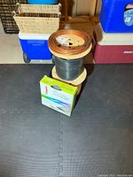Stacked spools: copper tubing on top, black-sheathed cable mid, white CU wire spool bottom, with Legrand Corduct box in front