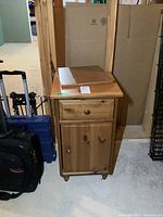 Front view of the manufactured wood end table showing top drawer and lower cabinet door with metal knob, some boxes and items next to it.