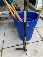 Photo showing Fiskar weed puller standing outside blue bucket with garden tools inside.