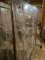 View of commercial garment rack with telescopic poles and plastic cover, showing the rack inside the dust cover in basement setting.