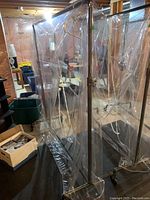 Commercial metal garment rack wrapped in clear plastic dust cover seen in basement setting with other items around.