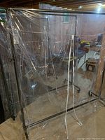Full view of commercial telescopic garment rack with clear plastic dust cover, showing metal frame and base on wheels.
