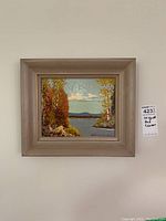 Framed oil painting of a water scene with autumn trees and mountains in the distance.