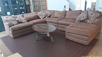 Full view of a brown microfiber sectional couch with six patterned throw pillows and a round coffee table in front