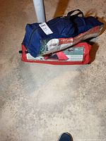 Two packed tents stacked on the floor, one blue bag labeled E-Z Tent Woods 7x7 and one red bag labeled Ozark Trail 9x8 dome tent.