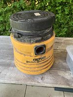 Yellow Genie 6 gallon wet/dry vacuum on wooden surface outdoors, showing body and top with coiled power cord.