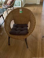 Wicker chair with metal frame and tufted dark gray cushion on hardwood floor, front angle view.