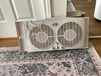 Full view of Hampton Bay dual fan window fan with expandable side pieces on a patterned carpet.