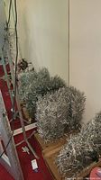 Five piles of silver tinsel branch segments on brittle cardboard boxes against wall.