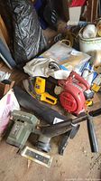 Wide view of the lot showing Black and Decker edger in foreground, red Homelite blower behind it, and other garage items