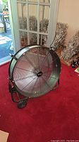 Front angle of black metal Utiltech Pro floor fan with protective grille and wheels on red carpet.