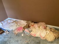 Wide view of assorted linens, doilies, and placemats spread on carpeted floor, showing mix of colors and textures