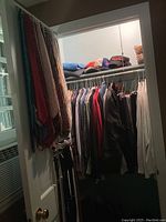 Closet with men's clothing on hangers including shirts, pullovers, coats, and ball caps on shelf above.