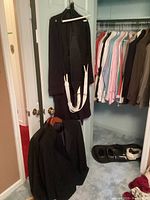 Black tuxedo jacket and pants with suspenders, arranged hanging and on floor before closet with dress shirts and coats
