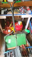 Photo of green Scott's spreader with orange wheels and black handles surrounded by various colored gas cans on the floor and under a workbench