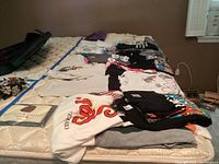 Full lot of assorted t-shirts folded and laid on bed, showing multiple graphic and plain shirts in various colors and styles.