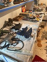 Photo of electric drills, three vises, and various tools laid out on a workbench covered with a towel.