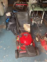 Full front view of red Troy-Bilt self-propelled lawn mower showing overall condition and rear collection bag with manual placed on it.