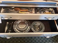 Drawer with pewter plates, two stands, and various kitchen utensils including wooden spoons