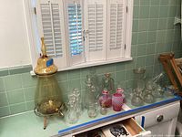 Wide view of all glassware on counter including amber urn, glass decanters, pitchers, stemware, and other items