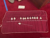 Twelve spoons laid out in red cloth roll-up case with one spoon removed.