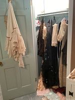 Vintage clothing and accessories hanging in closet and on door, including lace shawl, vintage dresses, and crocheted handbag.